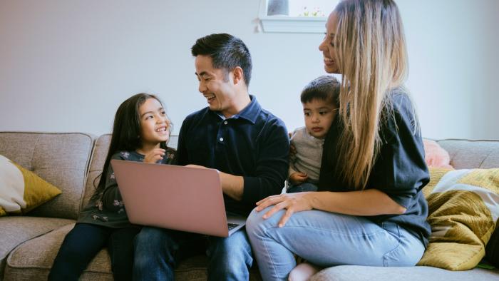 Family gathered around a laptop while sitting on a couch.