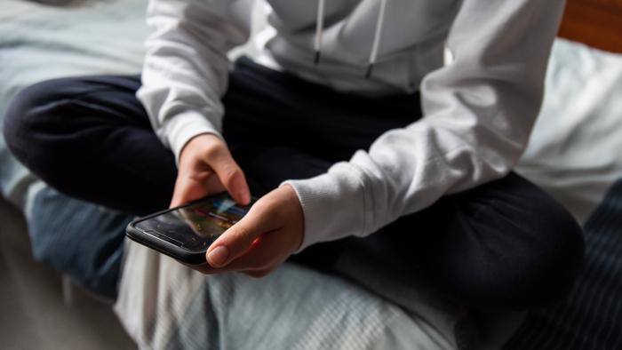 Kid sits cross-legged on bed looking at phone