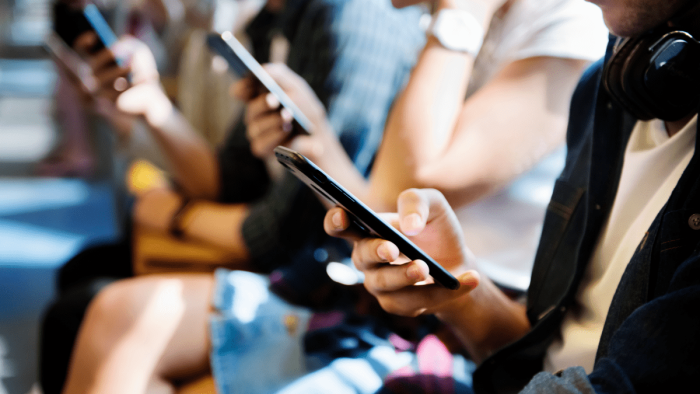 A line of teens are looking at their smart phones. 