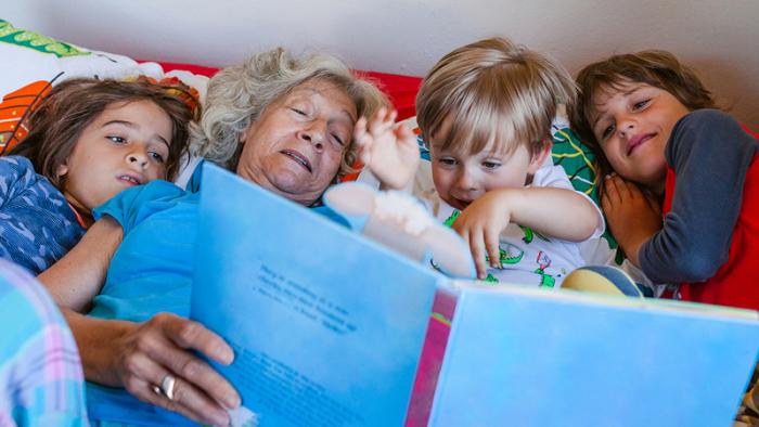 Grandmother reading a book to three children in bed.