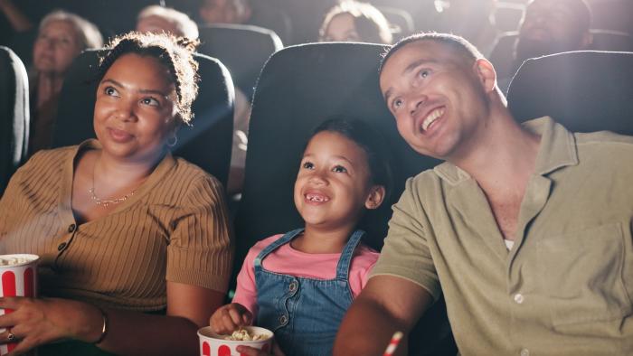 Family enjoying a movie in a theater, eating popcorn and smiling.