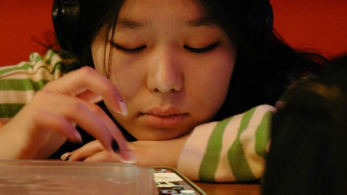 Young person with headphones touching a tablet screen, wearing a striped shirt.