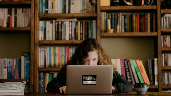 This is a photo of an adolescent child seated at a desk, their attention focused on a laptop screen.