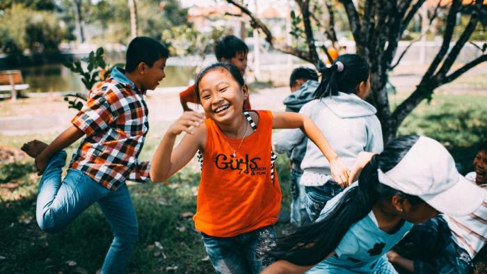 Children joyfully running and playing outside under trees.