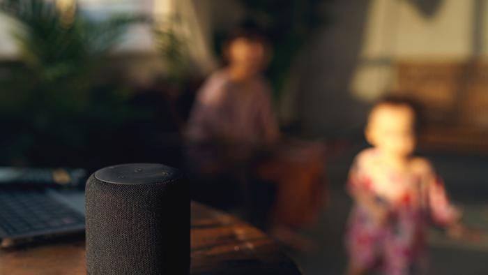 Young children blurred out behind the image of a smart speaker.
