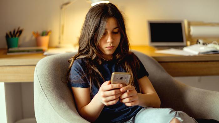 Young girl curled up in a chair looking at her phone.