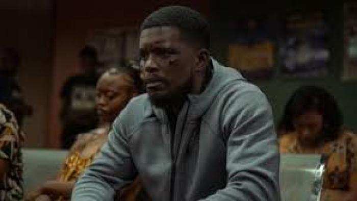 180 scene 2: Man in a gray hoodie sits pensively in a room with others.