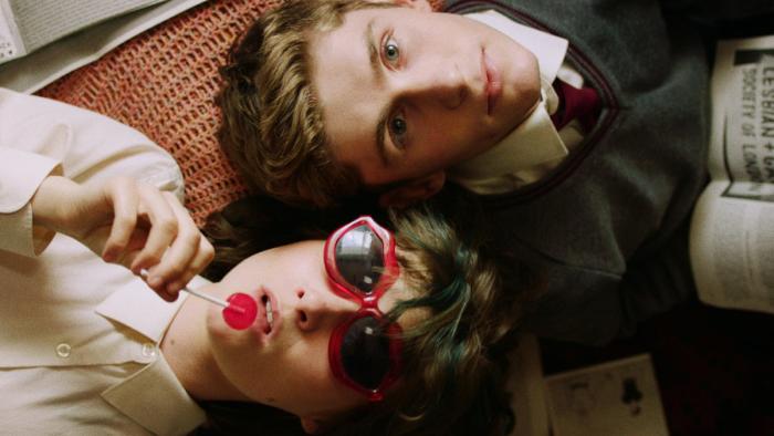 Dating Amber movie: Eddie and Amber lie with heads close, Amber coolly holding a red lollipop with sunglasses