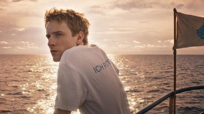 23 000 Lives movie: Louis Hoffman stands at the railing of a ship overlooking the Mediterranean Sea at sunset