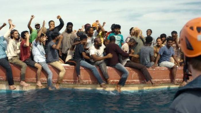 23 000 Lives movie: A group of people on a boat celebrate, with one person wearing an orange helmet in the foreground.