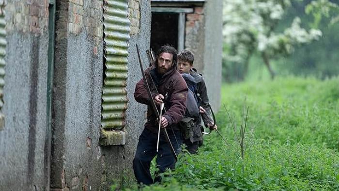 28 Years Later Movie: Jamie and his son, Spike, lurk outside an abandoned house, bows and arrows ready