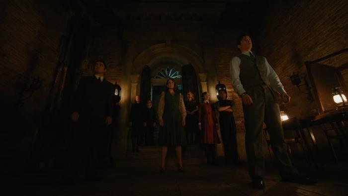 A Haunting in Venice Movie: Several people stand in a dark room, facing away from an adorned window