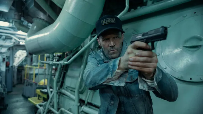 Mutiny: Shaved-headed man in denim jacket and cap aiming a gun aboard a ship