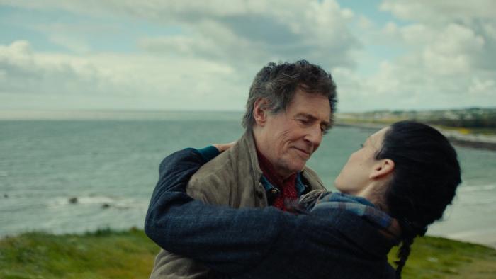 Death of a Ladies' Man: An older White man embraces a younger White woman next to a cliff's edge with the sea behind them