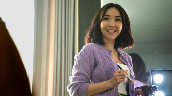 A Normal Woman: Erika stands holding a makeup brush and compact smiling broadly at someone off screen.