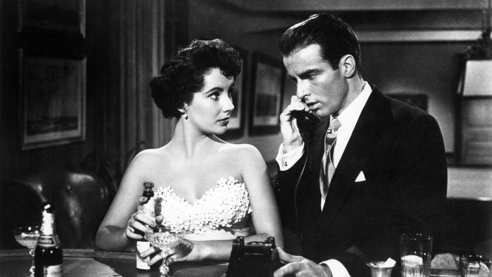 A Place in the Sun: Elizabeth Taylor, in a white dress, watches Montgomery Clift, in a black suit, as he makes a telephone call.
