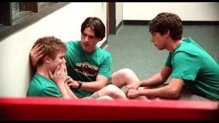 A Smile as Big as the Moon: Three boys in green shirts sit consoling each other in a hallway.