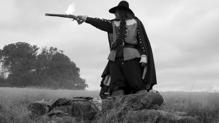 A Field in England: A man in 1600s British clothes fires a gun