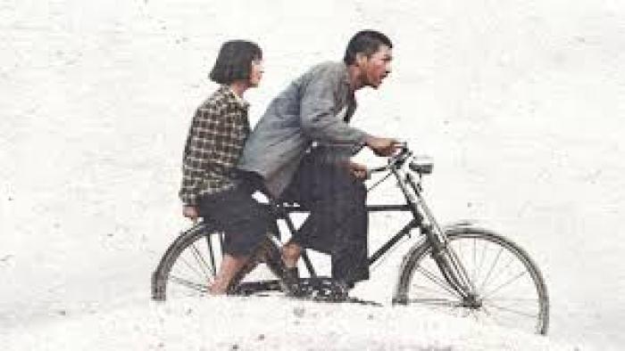A Foggy Tale: Man cycling with girl sitting on bike's rear, against light background.