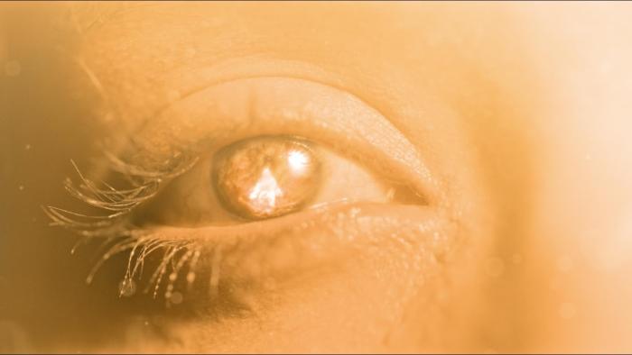 After Death Movie: A single human eye seems to be reflecting a brilliant, warm light, which also makes the person's skin glow