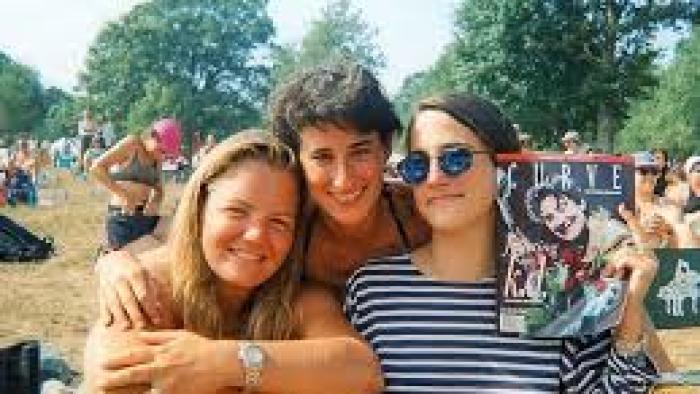 Ahead of the Curve: 3 women with arms around each other outside