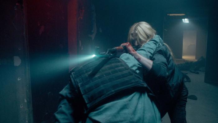 Air Force One Down Movie: Allison Miles (Katherine McNamara) fights with a terrorist in a dimly lit hallway; she uses a rifle fitted with a flashlight as leverage against his shoulder; his arm is around her neck