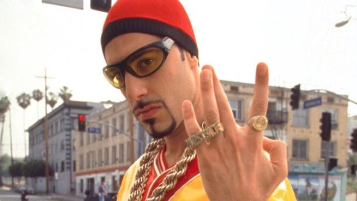Ali G InDaHouse Movie: Ali G in sunglasses and red beanie gesturing with rings in urban setting