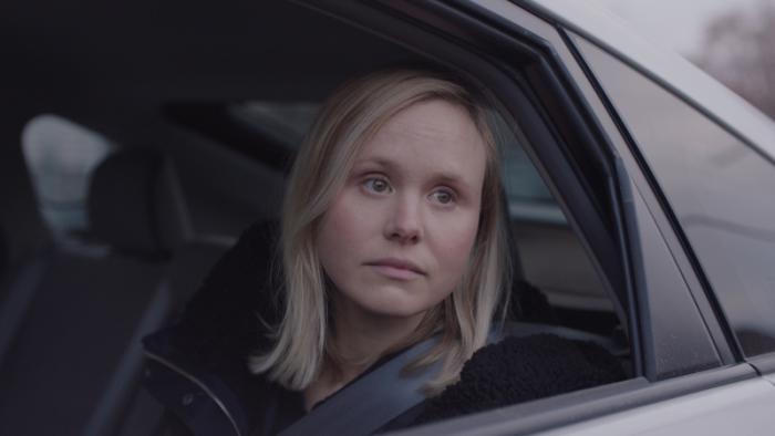 A woman looks out of the driver's side window of a car.