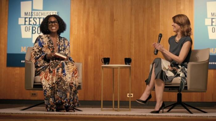 American Fiction Movie: Issa Rae sits with a speaker as she talks about a book
