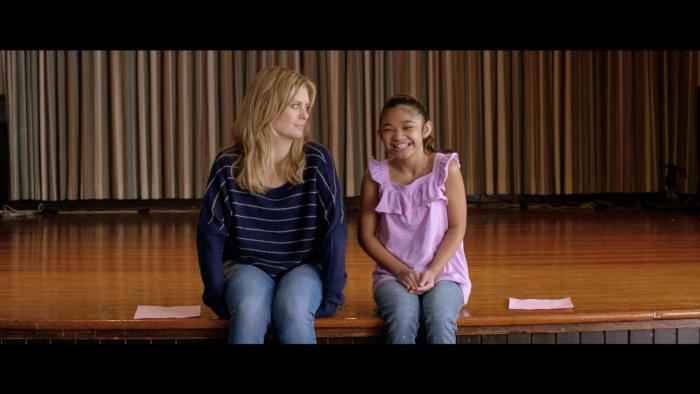 Kay and Anna sit together on the edge of an empty stage.