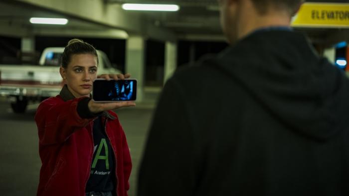American Sweatshop Movie: Daisy holds her phone accusingly out to a stranger in a parking garage