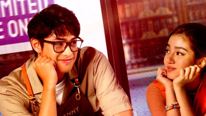 An Inconvenient Love: Sitting Filipino man in glasses left looks at Filipino woman with hands under chin as she looks back