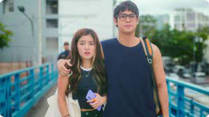 An Inconvenient Love: On walkway Filipino man in glasses and dark blue shirt on right has arm around Filipino woman in black shirt and neckless holding cell phone on left
