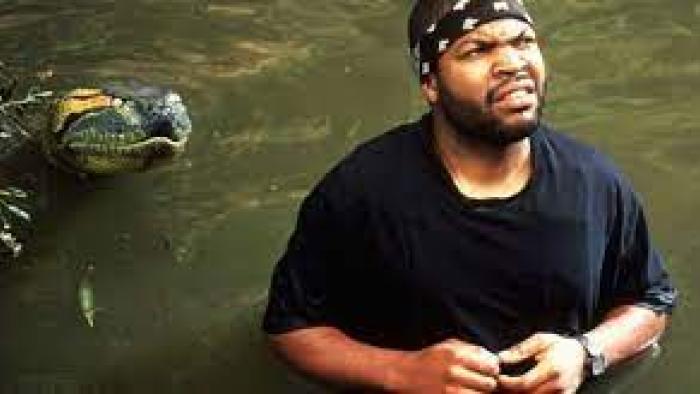 Anaconda Movie: Danny scrunches his face while wading in waist-high brown water, a snake behind him