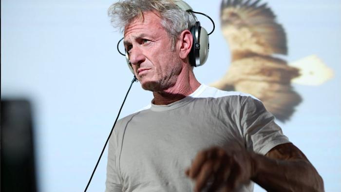 Animals in War: Sean Penn stands with headphones on his head with a clip of an eagle behind him