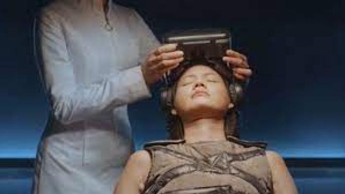 Arini by Love.inc: An Indonesian woman in white left puts a virtual reality headset on Indonesian woman with eyes closed center who is lying back on chair facing upward