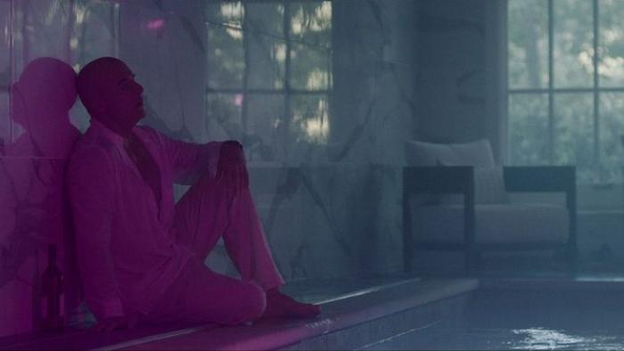 Assassin Movie: Adrian sits by a swimming pool, bathed in purple light and looking distraught