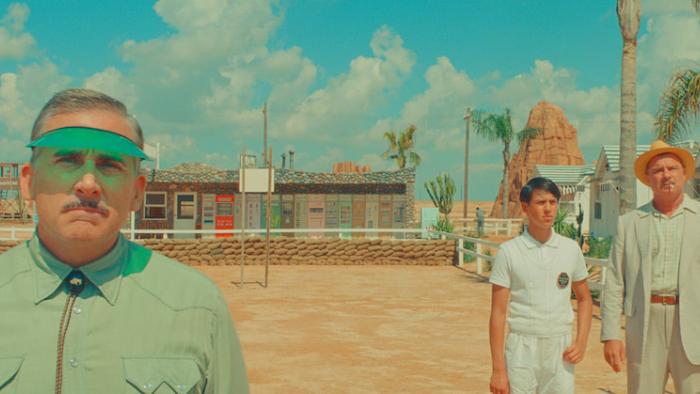 Asteroid City Movie: Standing in a desert are a White man in his 50s with a thin mustache wearing a green shirt and matching visor looking straight ah