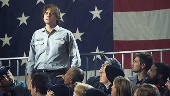 Atlas Shrugged III: Man in a crowd standing in front of a large American flag.