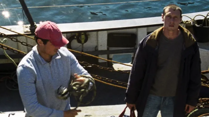  Two men on a boat, one holds a fishing rod, the other looks forward