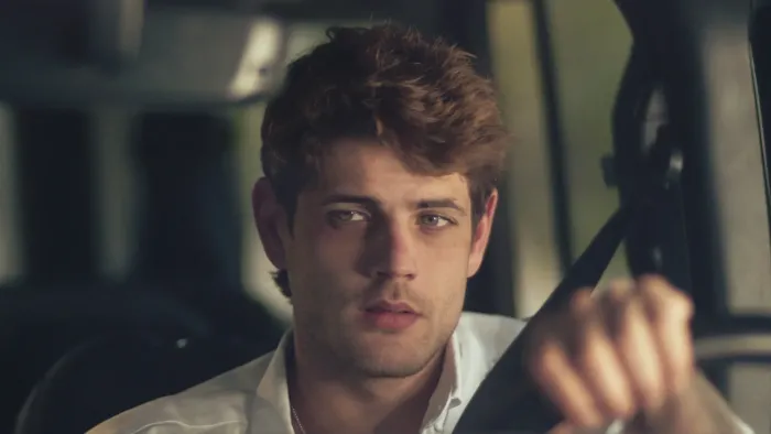Bad Influence movie: White Spanish young man with short brown hair and in white shirt center grips steering wheel while in driver seat of car
