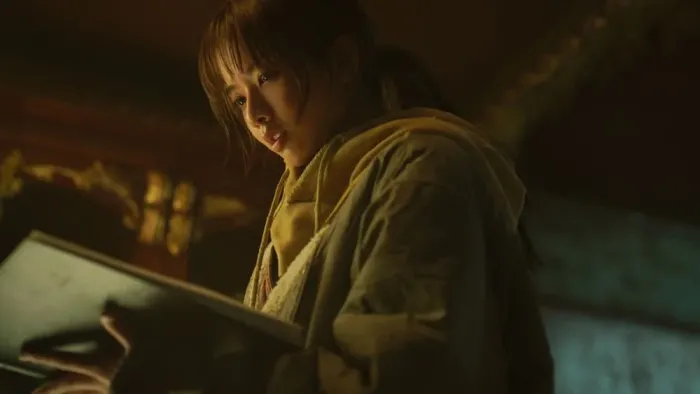 Badland Hunters movie: Korean woman center looks down at an open book in her hands