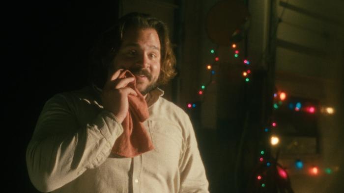 The Baltimorons Movie: Cliff (Michael Strassner) smiles, holding a towel to his cheek, with holiday lights behind him