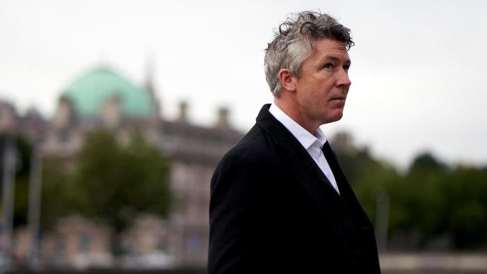 Barber: Aidan Gillen wears a black coat and white shirt as he stands outside with a building behind him