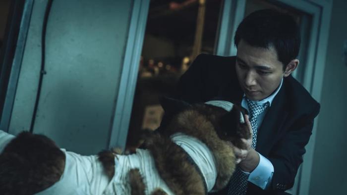 Believer 2 movie: Korean man in suit and tie right holds bandaged dog's face