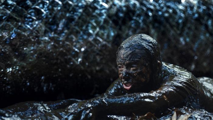Beware Boiúna movie: A person covered in mud next to a large, scaly creature