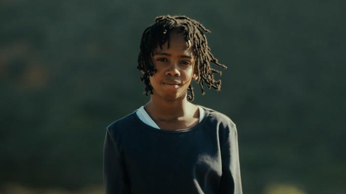 Bird Boy movie: An African boy stands outside with a deflated look on his face
