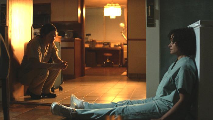Birth/Rebirth Movie: Rose (Marin Ireland, left) squats against a door and talks to Celie (Judy Reyes) who sits on the floor
