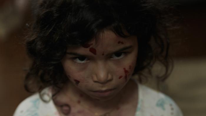 Birth/Rebirth Movie: Little Lila (A.J. Lister) has spatters of blood on her face and an expression of menace