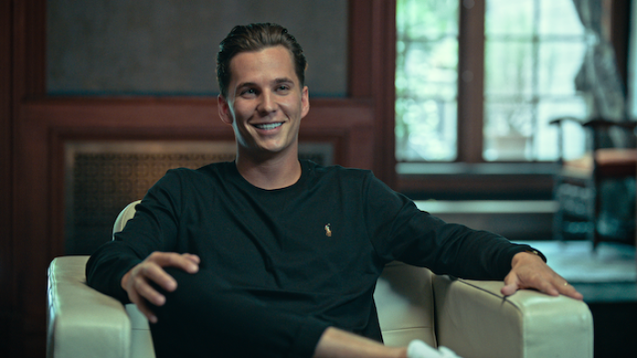 Still from Bitconned: Raymond Trapani, Centra Tech's chief operating officer and co-founder, sits in a chair for an in-person interview, wearing casual sports attire that includes a black long-sleeved top and matching pants 